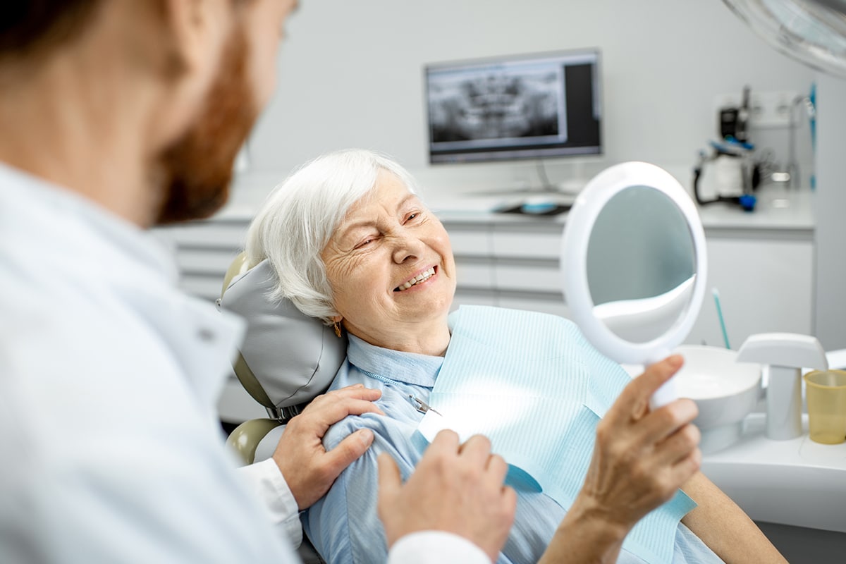 mature woman in dental chair smiling while holding mirror